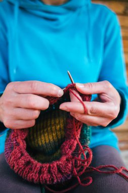 Kadın yün iplikten bir şapka örüyor. Kadın eli, yakın plan. El yapımı. Renkli iplik ve örgü iğneleri.