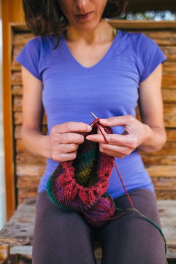 Kadın yün iplikten bir şapka örüyor. Kadın eli, yakın plan. El yapımı. Renkli iplik ve örgü iğneleri.