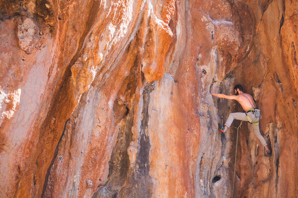 A strong man climbs a cliff. Climber overcomes a difficult climbing route on a natural terrain. Rock climbing in Turkey. Beautiful orange rock.