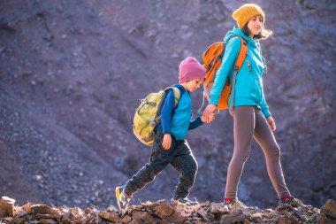 Bir kadın bir çocukla seyahat ediyor. Anne ve oğlu dağlarda. Çocuklarla birlikte dağın tepesine tırman. Sırt çantalı çocuk tepeye tırmandı. Etkin tatiller.