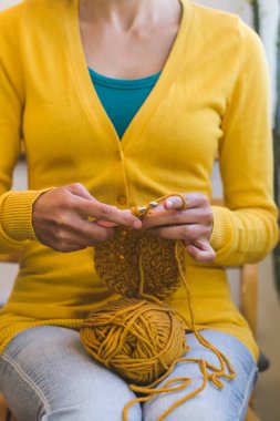 Kadın örgü örüyor. Kadın eli, yakın plan. Kız dikiş işiyle meşgul. Bir top sarı iplik ve örgü kancası..