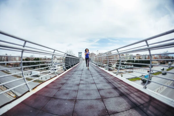 A woman runs across the bridge over the road. Running training in the city. Girl trains endurance. Jogging. Reaching the goal. Workout. City landscape.