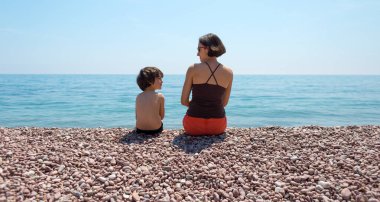 Annesiyle kumsalda oturup denize bakan bir çocuk. Bir kadın oğluyla birlikte okyanus kıyısında dinleniyor. Bir çocuk annesiyle vakit geçirir. Bir çocukla seyahat et..
