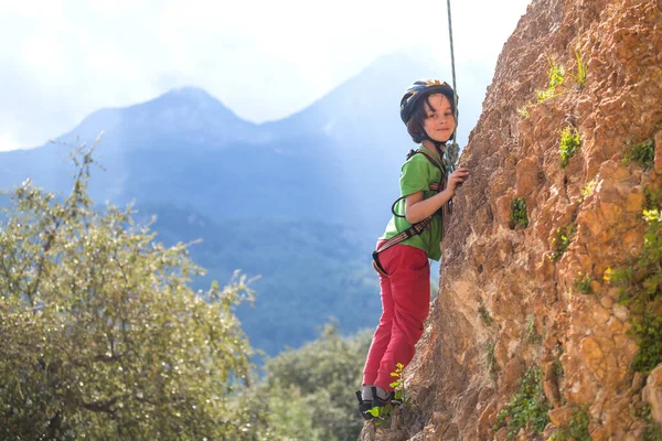 子供は自然の地形に登っています 少年は山を背景に岩に登る 趣味は アスレチックキッズの列車が強いです ロッククライミングの安全性 — ストック写真