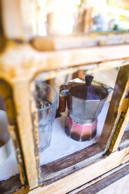Eski çizik bir gayzer kahve makinesi pencerenin yanında duruyor. Eski bir ahşap evin pencere eşiğinde cam ve gayzer kahve makinesi..