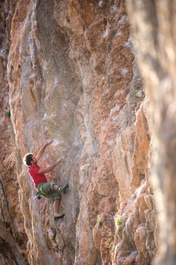 Güçlü bir adam uçuruma tırmanır. Dağcı, doğal bir arazide zorlu bir tırmanış rotasının üstesinden gelir. Türkiye 'de kaya tırmanışı. Güzel turuncu kaya.