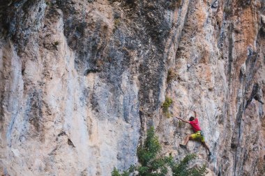 Güçlü bir adam uçuruma tırmanır. Dağcı, doğal bir arazide zorlu bir tırmanış rotasının üstesinden gelir. Türkiye 'de kaya tırmanışı. Güzel turuncu kaya.