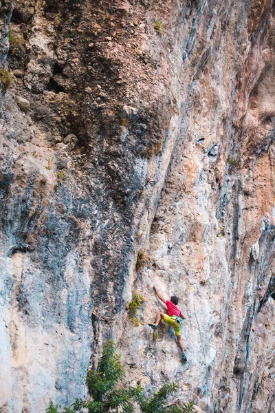 A strong man climbs a cliff. Climber overcomes a difficult climbing route on a natural terrain. Rock climbing in Turkey. Beautiful orange rock.