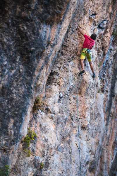 A strong man climbs a cliff. Climber overcomes a difficult climbing route on a natural terrain. Rock climbing in Turkey. Beautiful orange rock.