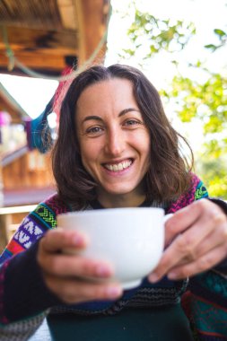 Kazaklı bir kadın kırsal bir ahşap evin verandasında sabah kahvesi içiyor. Gülümseyen kız verandada sabah içkisini içiyor..