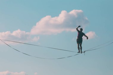 Mavi gökyüzünün arka planındaki Highliner bir hamle yapar. Bir adam uzatılmış bir askıda yürüyor. Performans ipi yürüteç. İnsan, abyss üzerinde dengeler. İleriye doğru kararlı bir adım.