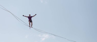 Mavi gökyüzünün arka planındaki Highliner bir hamle yapar. Bir adam uzatılmış bir askıda yürüyor. Performans ipi yürüteç. İnsan, abyss üzerinde dengeler. İleriye doğru kararlı bir adım.
