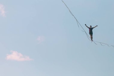 Mavi gökyüzünün arka planındaki Highliner bir hamle yapar. Bir adam uzatılmış bir askıda yürüyor. Performans ipi yürüteç. İnsan, abyss üzerinde dengeler. İleriye doğru kararlı bir adım.