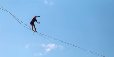 Mavi gökyüzünün arka planındaki Highliner bir hamle yapar. Bir adam uzatılmış bir askıda yürüyor. Performans ipi yürüteç. İnsan, abyss üzerinde dengeler. İleriye doğru kararlı bir adım.
