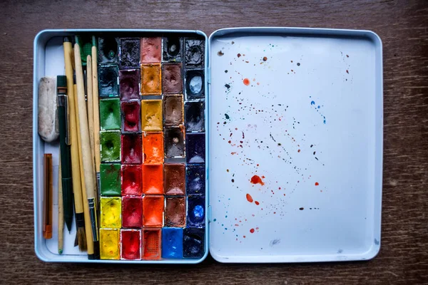 Set of watercolor paints and brushes on a wooden table, Multi-colored paints for drawing, Palette, Set for the artist.