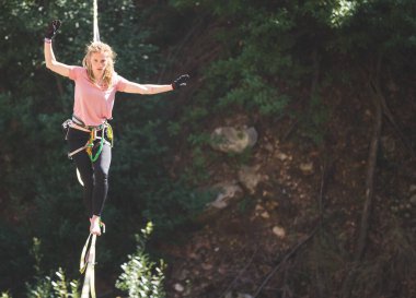 Bir kadın gerilmiş askı boyunca yürüyor. Dağlarda yüksek bir yer. Kadın dengeyi yakalar. Doğada ip cambazı performansı..