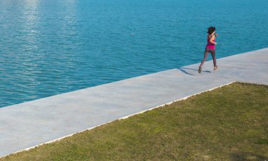 Bir kadın nehir boyunca şehir güvertesinde koşuyor. Kız yarış için antrenman yapıyor. Şehirde spor haberleri. Sahilde koşuyor. Koşucu maratona hazırlanıyor. Egzersiz.
