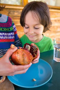 Mavi bir tabakta olgun, sulu bir nar. Bir çocuk nar tohumu yer. Sağlıklı meyve ikiye bölünür..