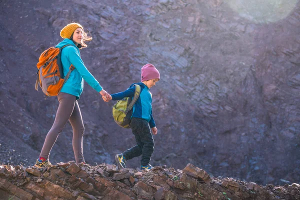 A woman is traveling with a child. Mom and son in the mountains. Climb to the top of the mountain with children. The boy with the backpack climbed to the top. Active vacations.