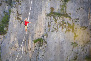 Bir adam gerilmiş askı boyunca yürüyor. Dağlarda yüksek bir yer. İnsan dengeyi yakalar. Doğada bir ip cambazının performansı. Dağların arka planındaki dağcı..
