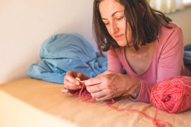 Kadın yatakta örgü örüyor, kadın elleri şapka örüyor, karantina sırasında yaratıcılıkla meşgul, el yapımı, favori ev hobisi....