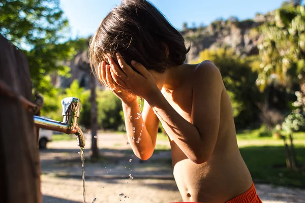 熱に疲れて 子供は家の中庭のタップから水で顔を洗う その少年は水道水を飲まされる 暑い夏 スプレー 村での休暇 — ストック写真