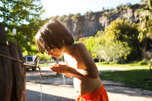 熱に疲れて 子供は家の中庭のタップから水で彼の体を洗う その少年は水道水を飲まされる 暑い夏 スプレー 村での休暇 — ストック写真