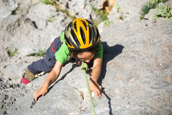 子供は自然の地形に登っています ヘルメットを被った少年が山を背景に岩を登る 趣味は アスレチックキッズの列車が強いです ロッククライミングの安全性 — ストック写真