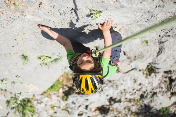 子供は自然の地形に登っています ヘルメットを被った少年が山を背景に岩を登る 趣味は アスレチックキッズの列車が強いです ロッククライミングの安全性 — ストック写真