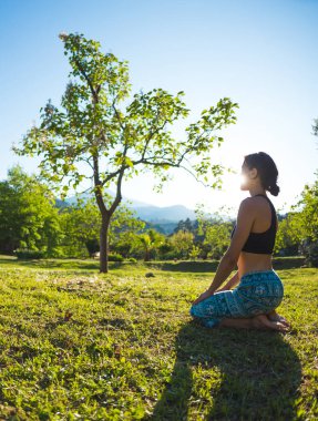 Kız yeşil çimlerde, yeşil ağaçların ve dağların arka planında yoga yapıyor, gün batımında asma dansı yapıyor, doğada meditasyon yapıyor, dengenin gelişmesi için egzersiz yapıyor..