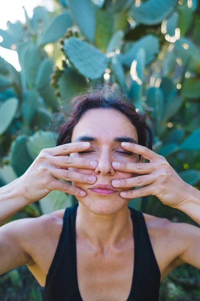 Woman does self-massage of the face, The girl practices yoga on the green grass on a background of green trees, A woman performs asanas at sunset, Meditation in nature, Female fingers on the face.
