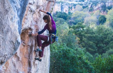 Bir kız ormanın arka planında bir kayaya tırmanır, atlet doğada antrenman yapar, kadın zor tırmanış rotasının üstesinden gelir, güçlü dağcı, aşırı hobi, Türkiye 'de kaya tırmanışı.