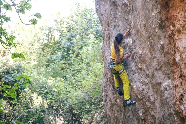 A girl climbs a rock on the background of the forest, The athlete trains in nature, Woman overcomes difficult climbing route, Strong climber, Extreme hobby, Rock climbing in Turkey.