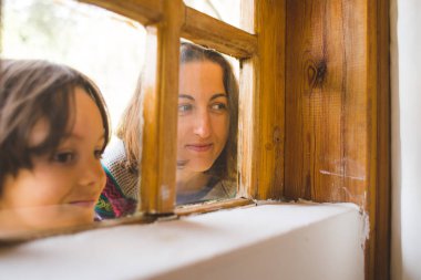 Annesiyle birlikte bir çocuk tuhaf bir şekilde ağaçtan bir evin penceresinden dışarı bakıyor, çocukların duyguları, çocuk camdan dışarı bakıyor..