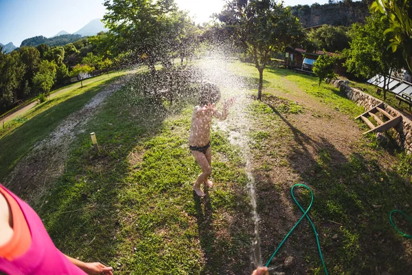 暑い晴れた日に水に浸かった少年 母は家の中庭にホースで子供を噴霧 休暇中のエンターテイメント 子供の感情 子供の楽しさ — ストック写真