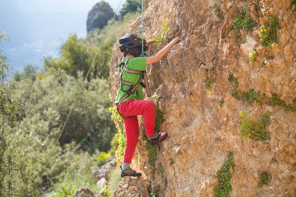 ヘルメットの子供は自然の地形に登っています 少年は山を背景に岩に登る 趣味は アスレチックキッズの列車が強いです ロッククライミングの安全性 — ストック写真