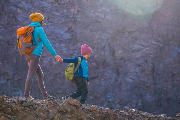A woman is traveling with a child. Mom and son in the mountains. Climb to the top of the mountain with children. The boy with the backpack climbed to the top. Active vacations.