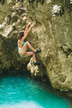 Mayo giymiş bir kadın, suyun üzerindeki bir uçuruma tırmanıyor, Türkiye 'de kayalara tırmanıyor, güçlü bir dağcı, doğal bir arazide antrenman yapıyor, derin su solosu..