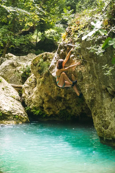 A woman in a swimsuit climbs a cliff above the water, Climbing over a mountain river, Bouldering in Turkey, A strong climber is training on a natural terrain, Deep water solo.
