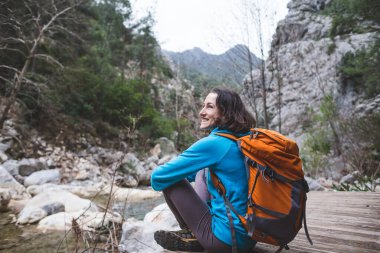 Sırt çantalı bir kadın eski ahşap bir evin verandasında oturur ve bir dağ nehrine bakar. Gezgin gece kalmak için bir kulübe buldu. Yürüyüşçüler için barınak. Manzaralı yerlerde geziyorum..