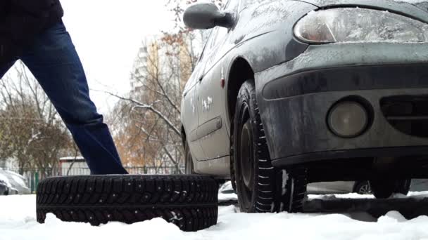 Человек кладет новые снежные шины рядом со старой машиной — стоковое видео