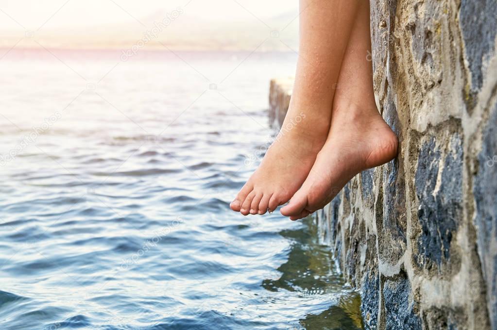 Bare girls feet dangling from the stone jetty