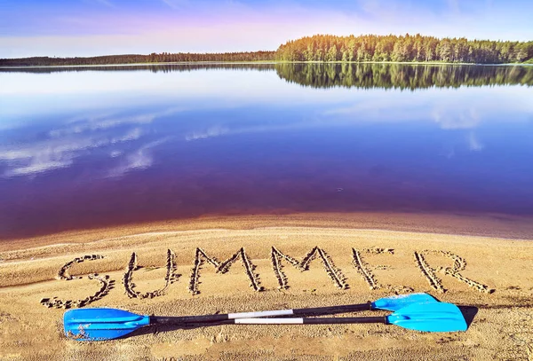 Kayak melat makaa järven rannalla lähellä sanaa kesällä kirjoitettu hiekkaan — kuvapankkivalokuva