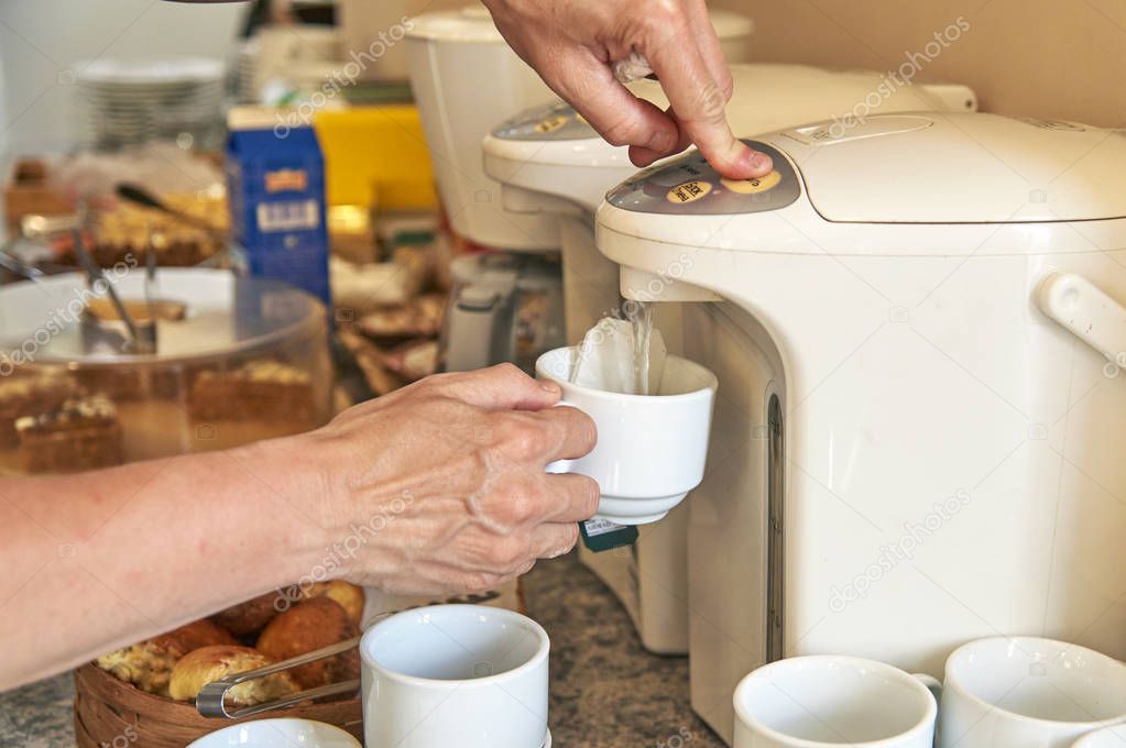 Woman brewing a tea from thermo pot in hotel kitchen
