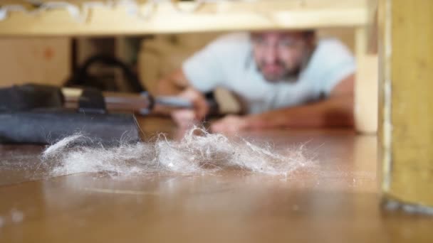 Мужчина чистит пол под кроватью пылесосом — стоковое видео