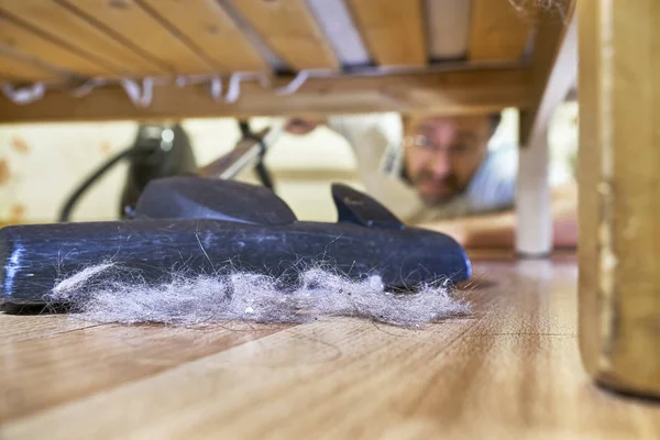 Мужчина чистит пол под кроватью пылесосом — стоковое фото