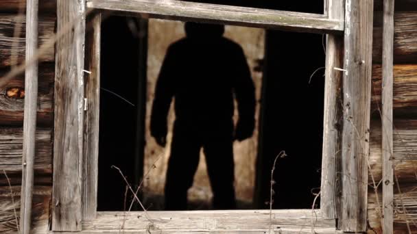 Silueta masculina de pie en una puerta oscura de una casa de madera abandonada destruida — Vídeo de stock