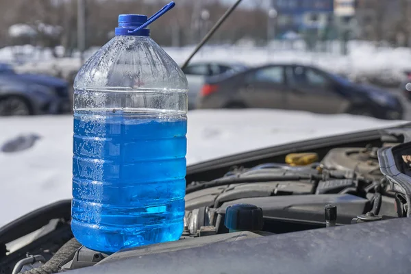 Kanister mit nicht einfrierender Flüssigkeit für Scheibenwaschanlage, der auf dem Motor eines Autos steht, das im Winter im Freien vor einer Straße steht — Stockfoto