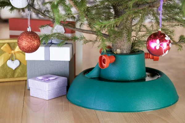 Yeni yıl arifesinde hediye kutularıyla çevrili plastik Noel ağacı standı evde duruyor.