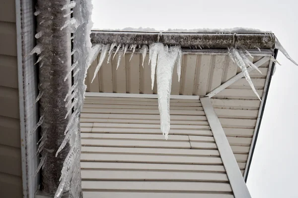 Långa istappar hänger på taket till ett hus på vintern Royaltyfria Stockfoton